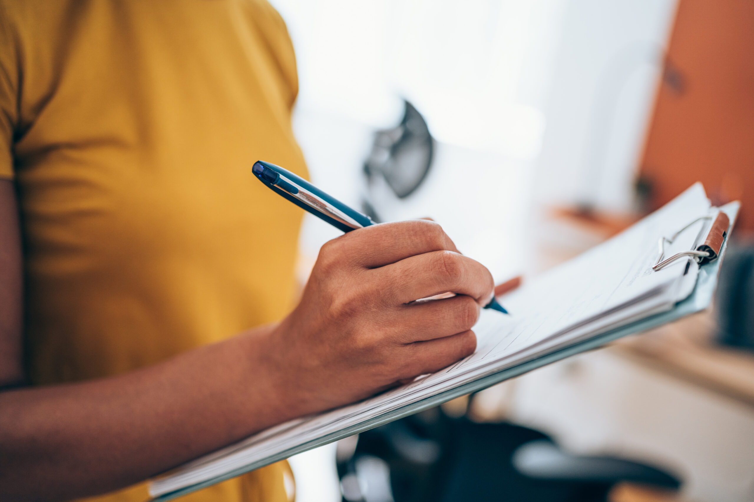 Person writing on clipboard with a pen.