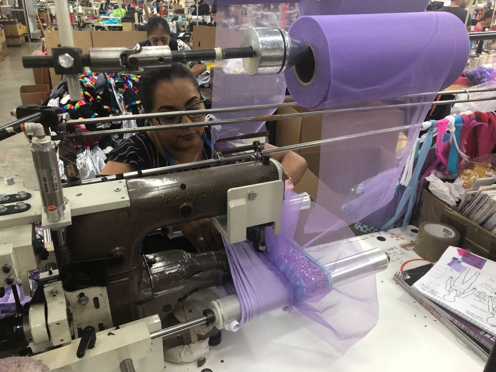A woman uses a large sewing machine to create a costume out of light purple tulle