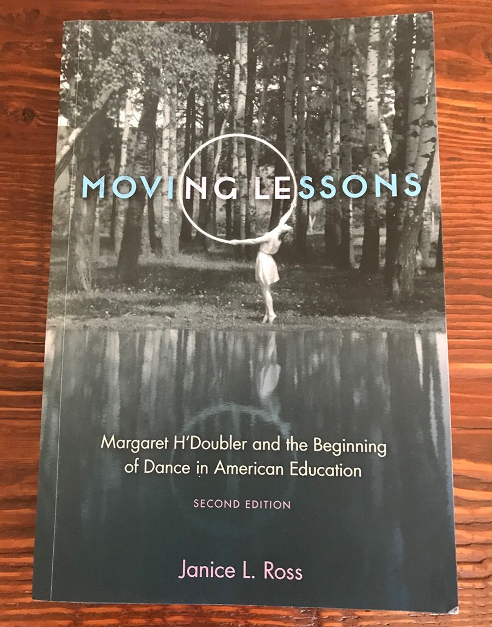The cover of Moving Lessons, featuring a black and white photo of a woman dancing outside with a large hula hoop-type prop