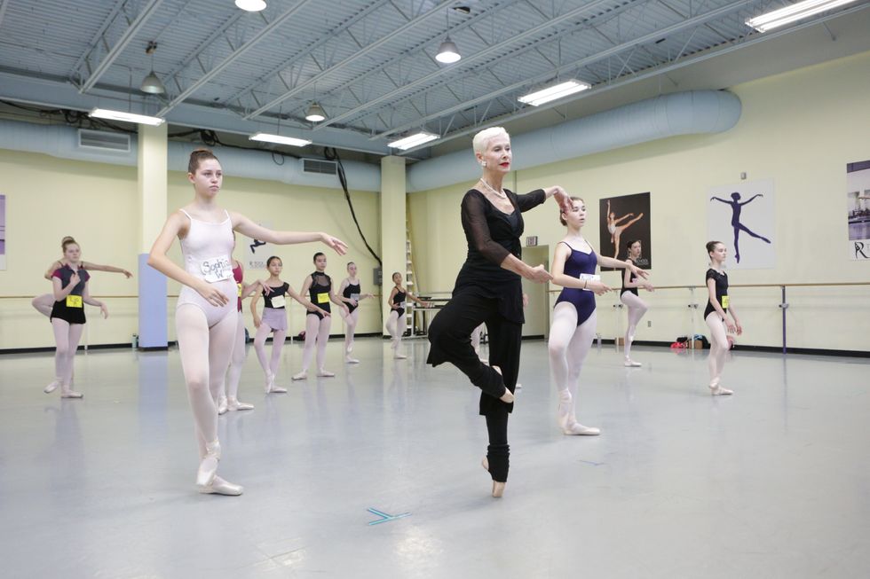 Stephanie, wearing all black and pointe shoes, demonstrates at the front of a classroom full of teenage girls