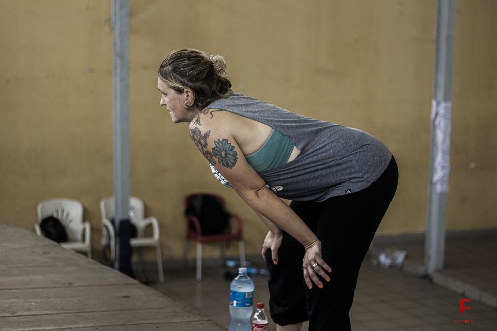 Abby Zbikowski leans over with her hands on her knees, looking off-camera intently. Her flower tattoo is visible on her bare shoulder.