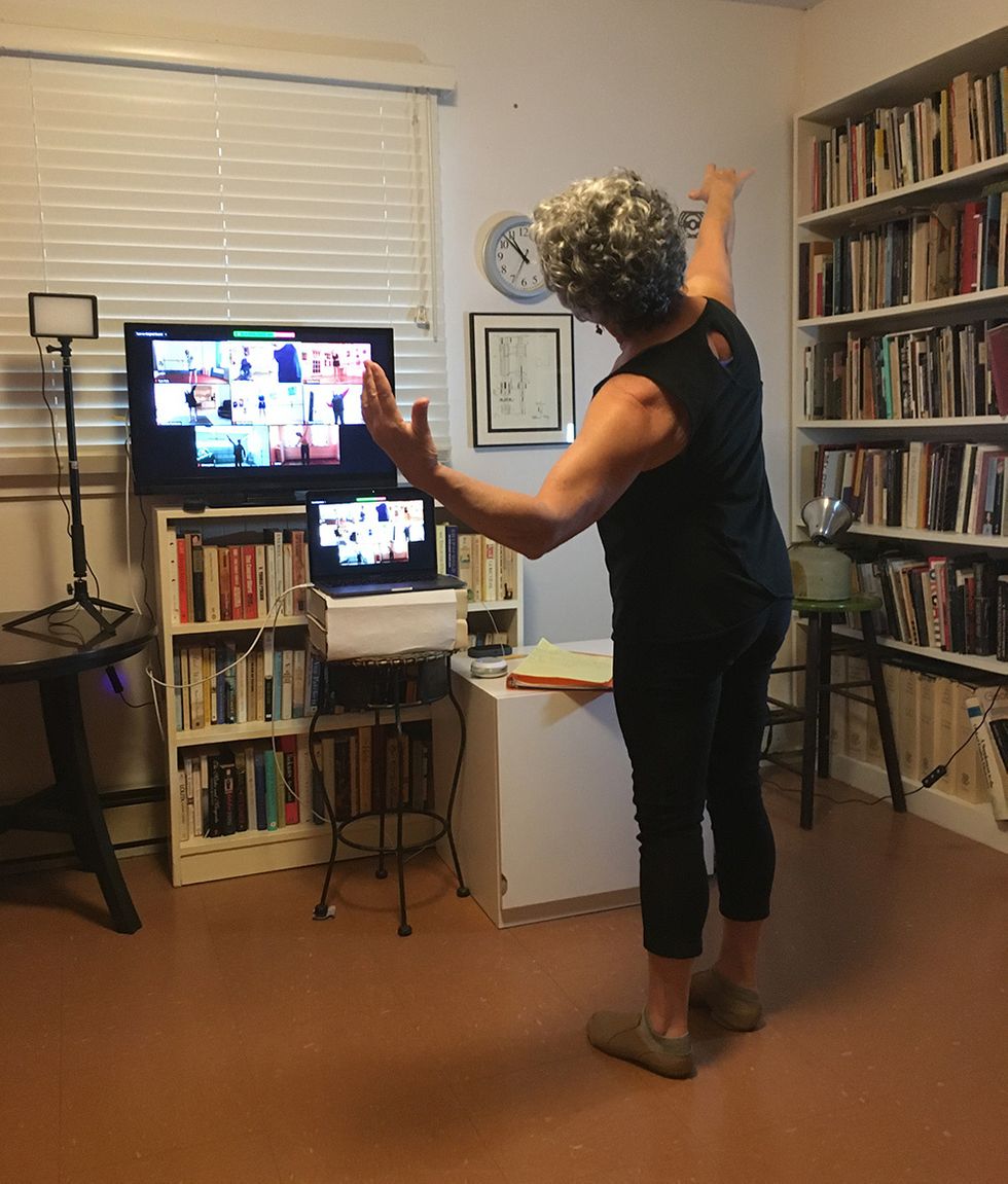 Koval, in her home, demonstrates in front of her computer, which shows a Zoom room full of students