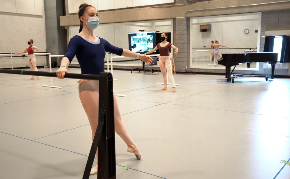 Masked ballet students spaced out in a barre do tendus