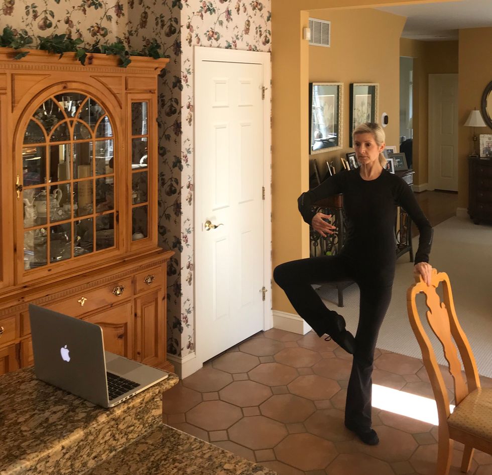 Elizabeth Ahearn teaches a virtual ballet class in her kitchen, in passe using her chair as a barre.