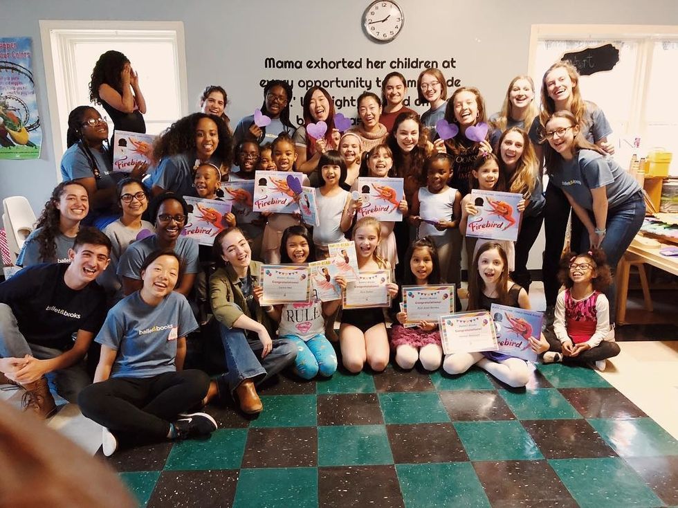 A classroom full of school children and young adult volunteers pose and smile for the camera. Some holding the book Firebird while others hold cut-out paper hearts or certificates.