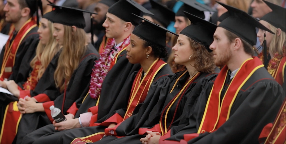 A row of students in cap and gowns listen to a graduation speech