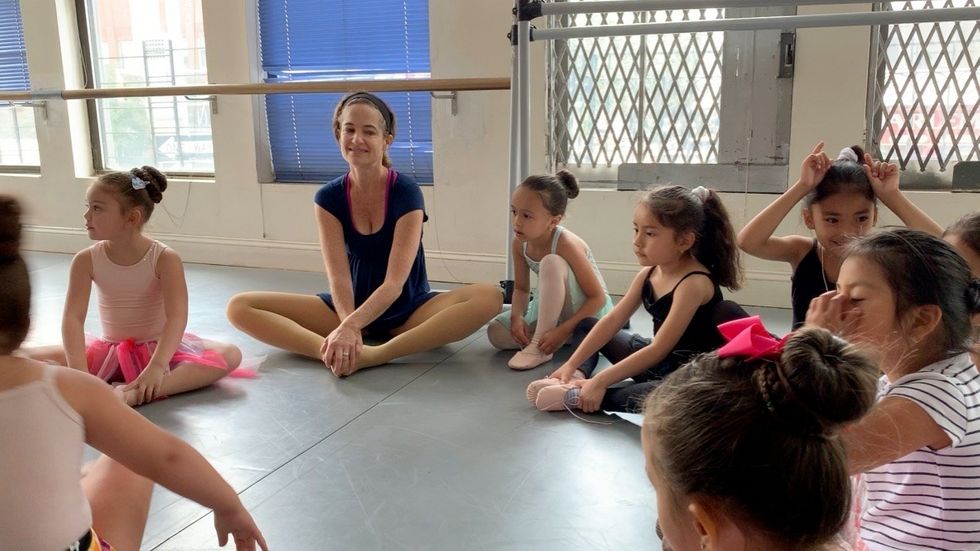 Abby McGreath sits on the floor stretching, surrounded by young students