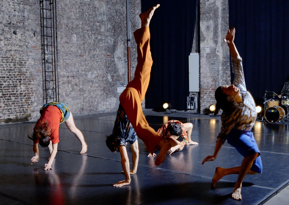 Four dancers in bright patterns and colors fall to the floor in gradual stages. One is mid-hand stand