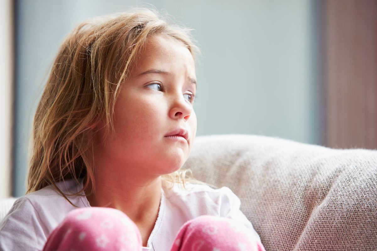 A young girl sits on her couch, looking sad