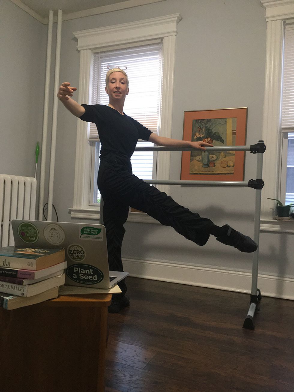 Rosner teaches at the small barre in her home, outside leg extended to degagu00e9, and smiling at the laptop screen.