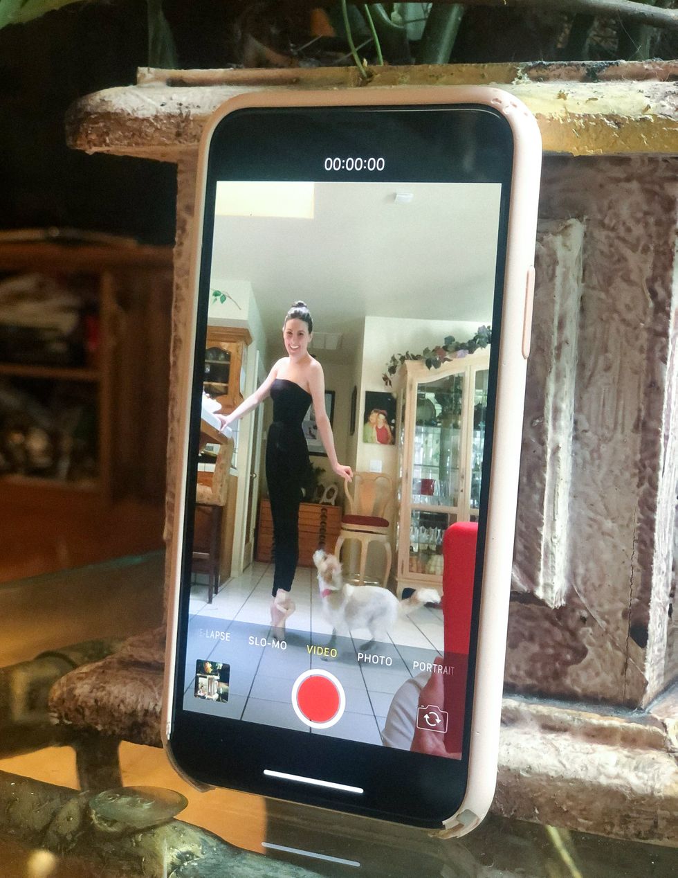 A smartphone, showing Tiler Peck standing on pointe in her living room with a dog, is propped up on a glass table.