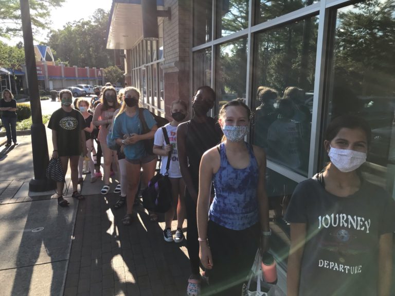 Teen stage door students line up outside the studio waiting to come in for class. They wear masks.
