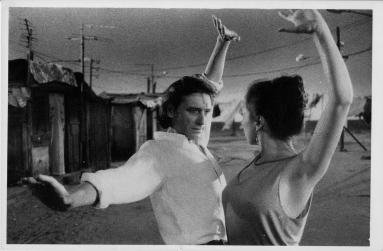 A black and white photo of a male and a female Flamenco dancer posing with their arms up, shown waist-up.