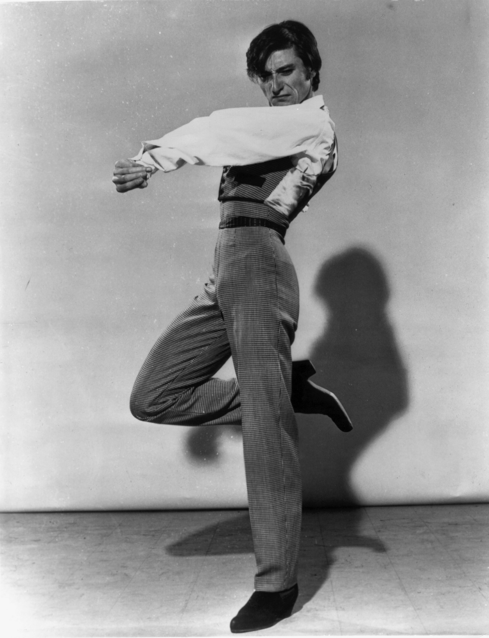 A black and white photo of a male Flamenco dancer, lifting his right leg and twisting his upper body with a passionate expression.