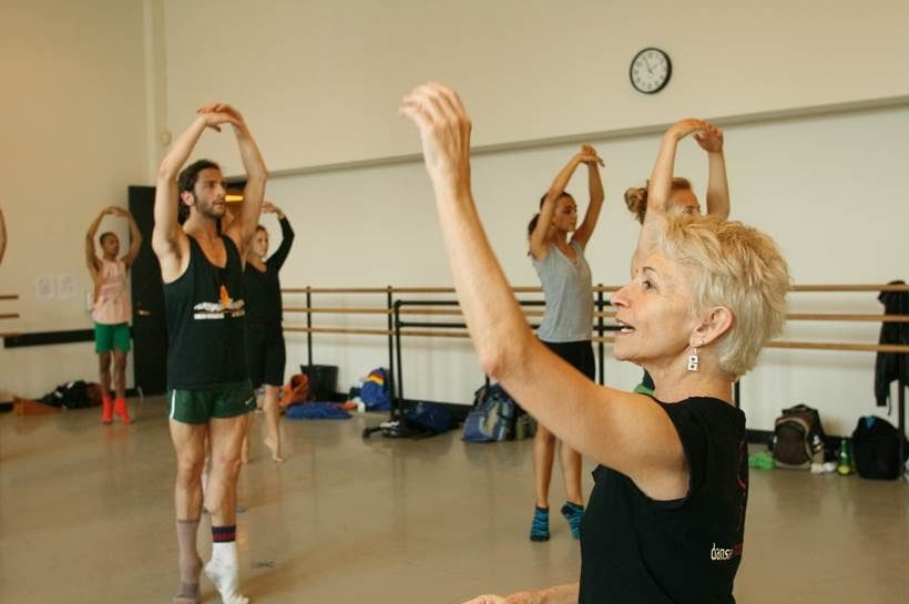 A woman dance teacher teaches class in a studio full of adult dancers.