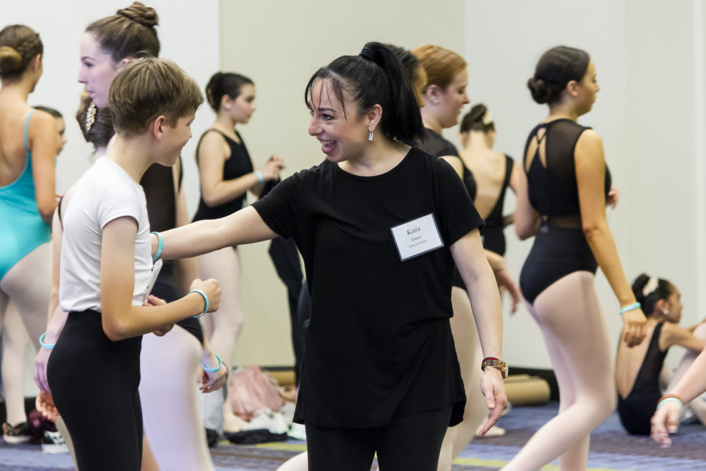 A dance teacher smiles while speaking with a junior-high-aged, male ballet dancer.