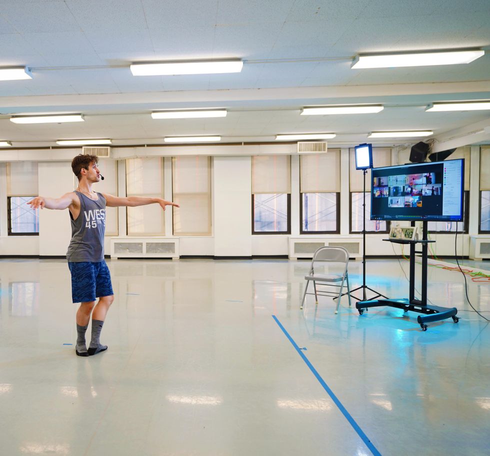 Barry Kerollis demonstrates a pirouette preparation from fifth position in an empty studio. He faces a large monitor showing Zoom screens.