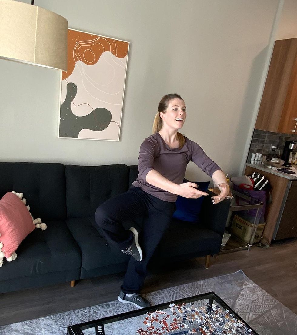 Shannon Oleson in passe in her living room, teaching a Zoom class. She is in front of her black couch, and behind a clear coffee table with an unfinished puzzle on it.