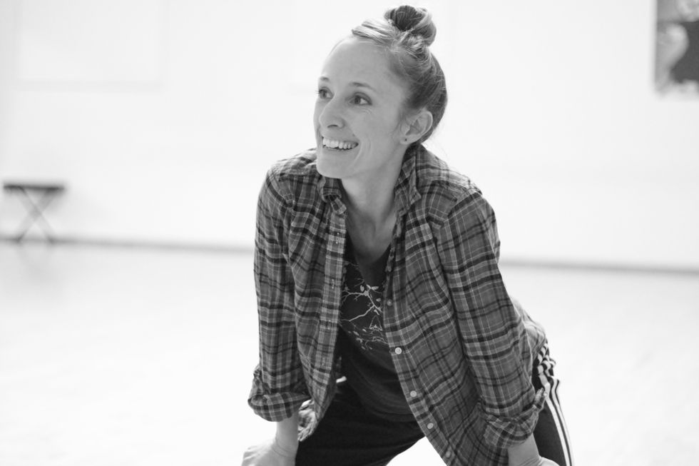 Katie Faulkner, wearing a flannel shirt, leans over with her hands on her legs, smiling