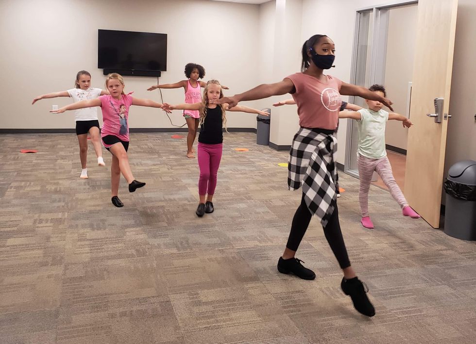 Lisa McCabe, who is masked, demonstrates a tendu as six young students dance behind her
