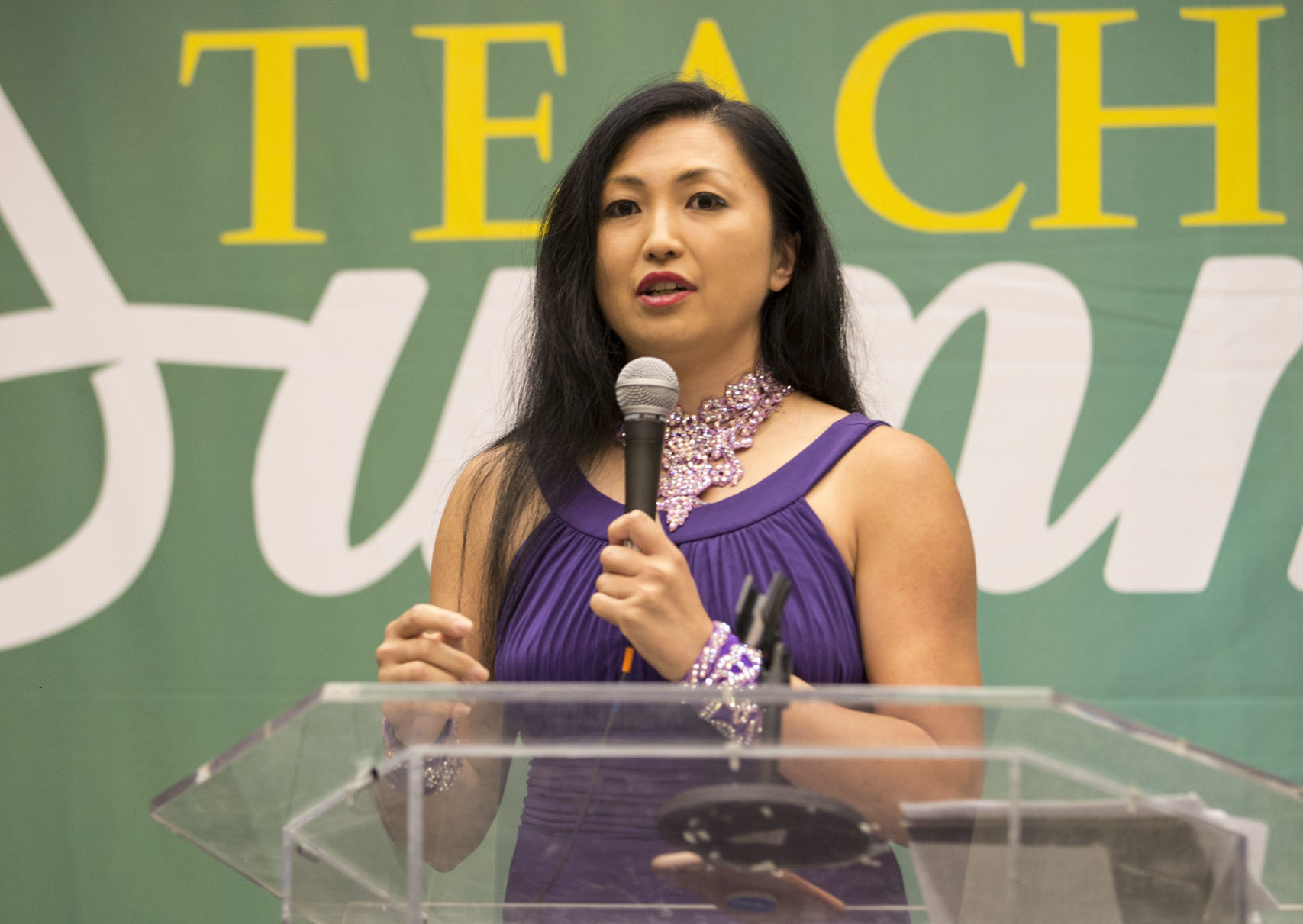 marisa hamamoto speaks into a microphone at a clear podium that reads "Dance Teacher Summit"