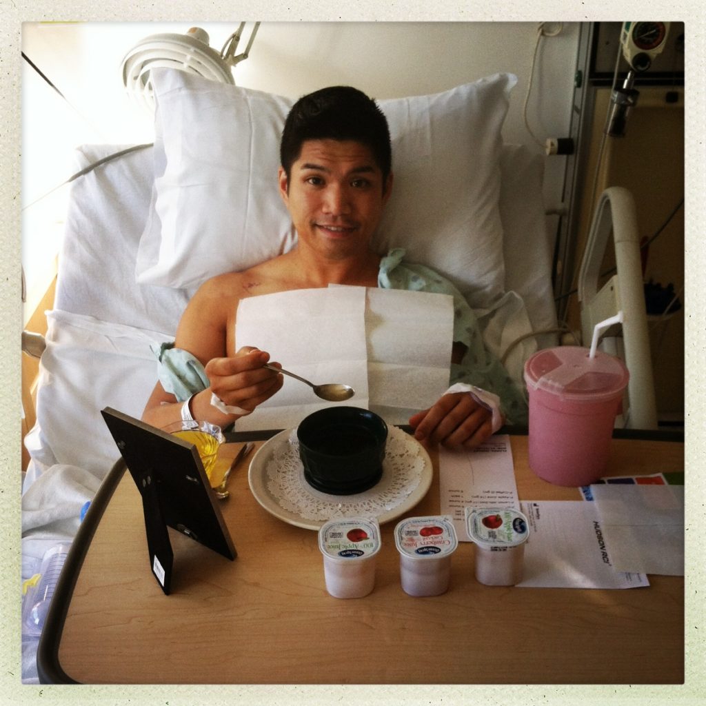 Dudley Flores lies in a hospital bed, eating from a tray