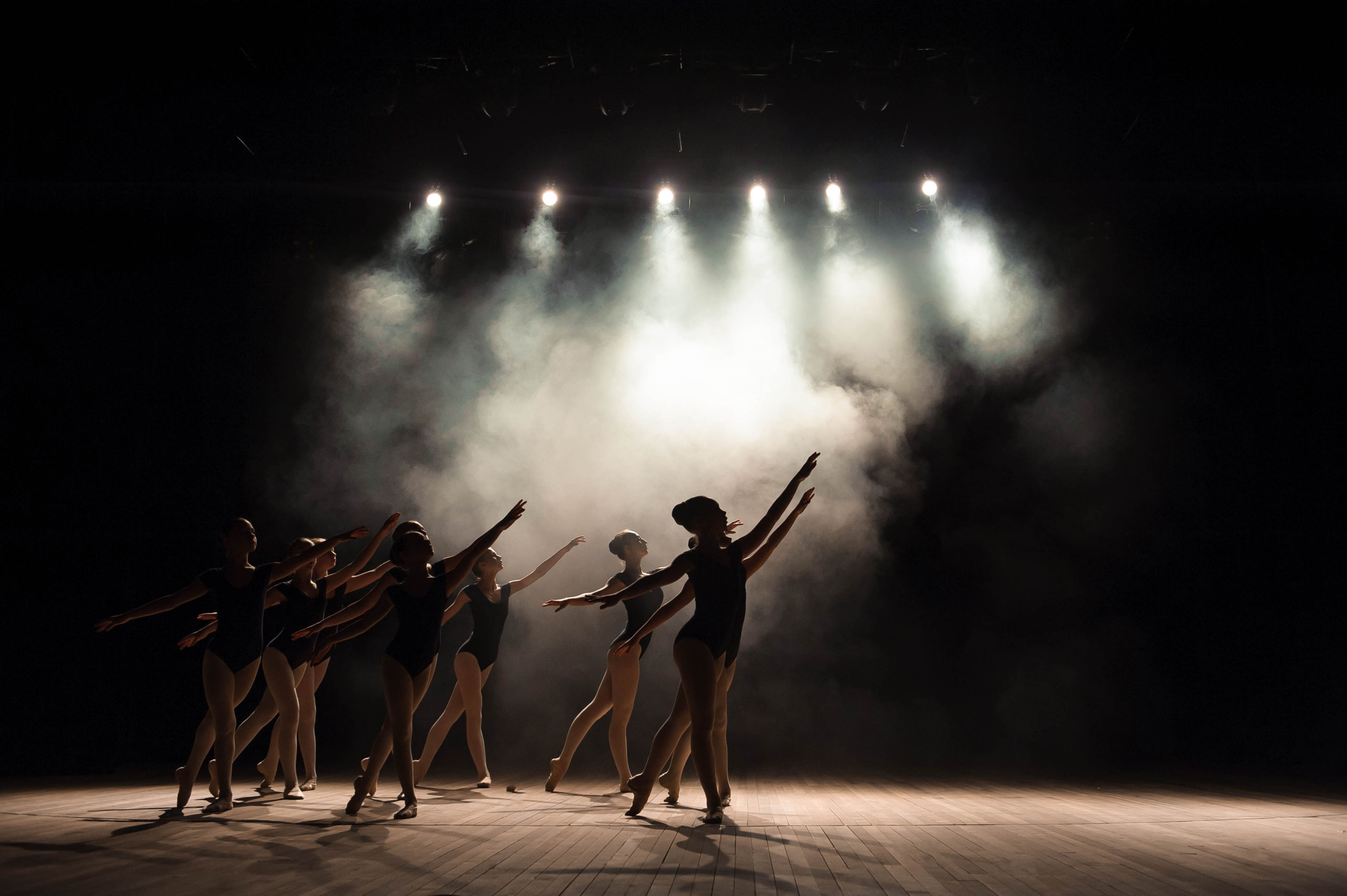 A group of ballet dancers on a smoky stage with dramatic lighting overhead.