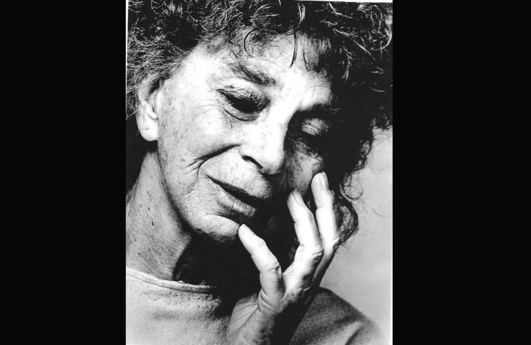Black and white headshot of Anna Halprin, looking down and holding her fingers gently to her cheek and chin