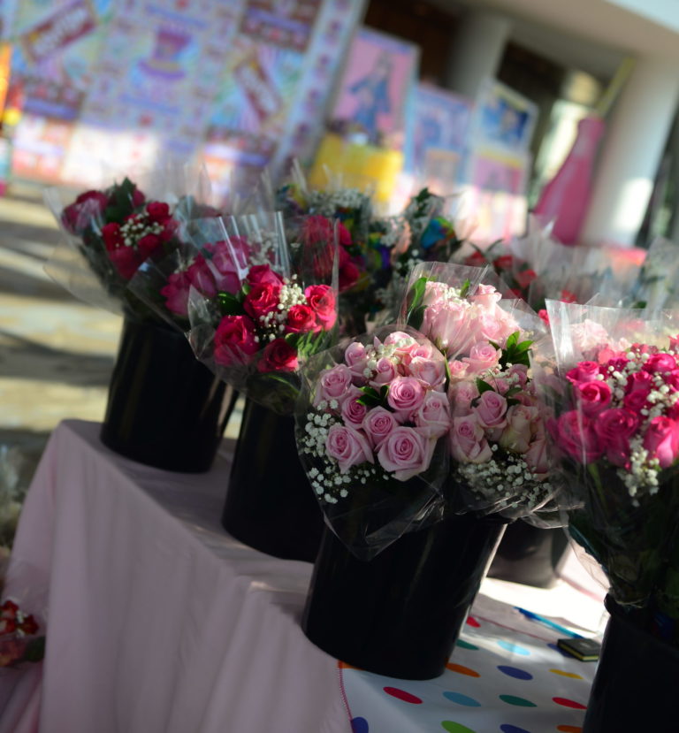 Buckets containing bouquets of flowers—mostly red and pink roses—sit on a table with a colorful tablecloth