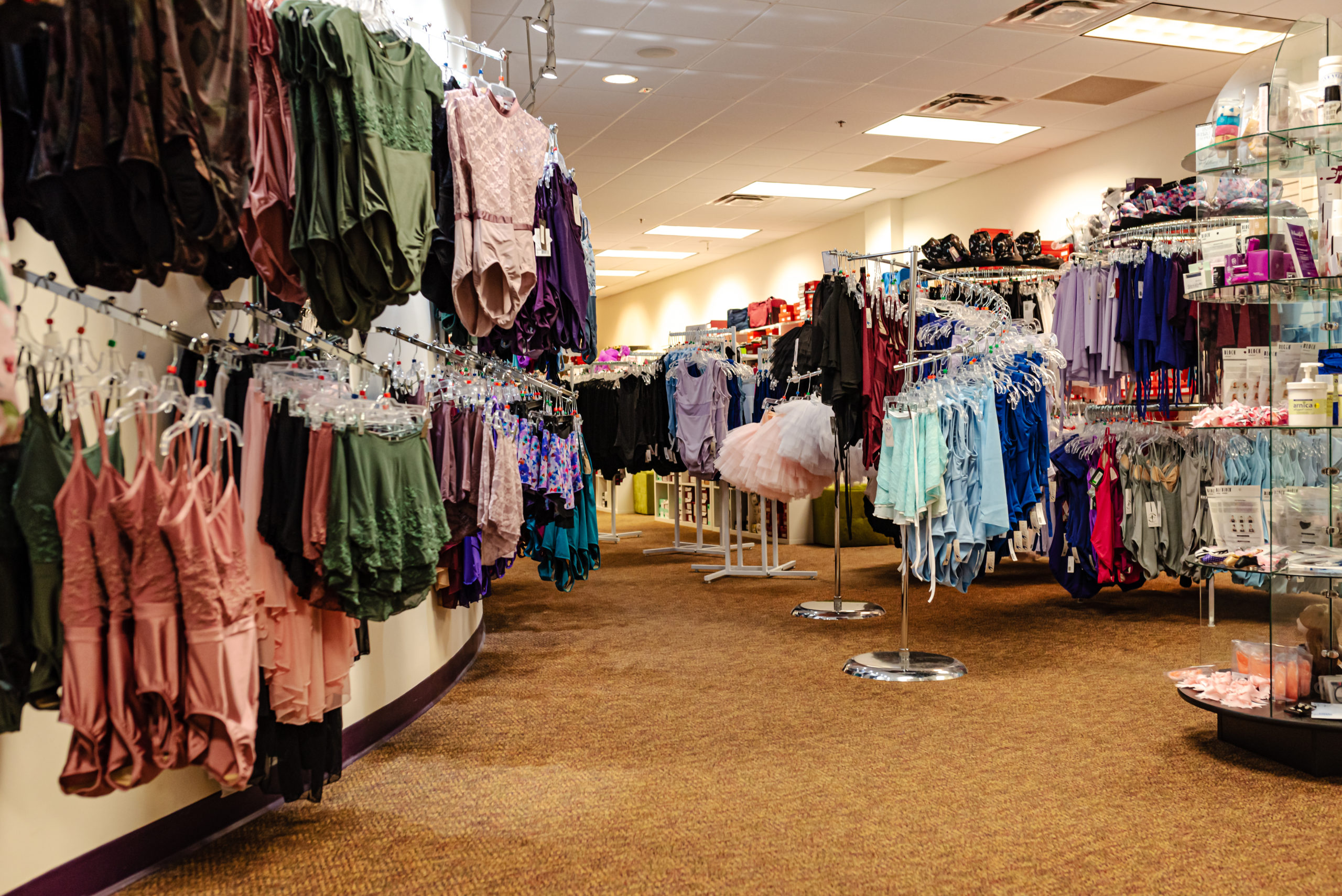A small dancewear store has racks and displays full of colorful leotards and skirts, as well as shelves full of accessories.