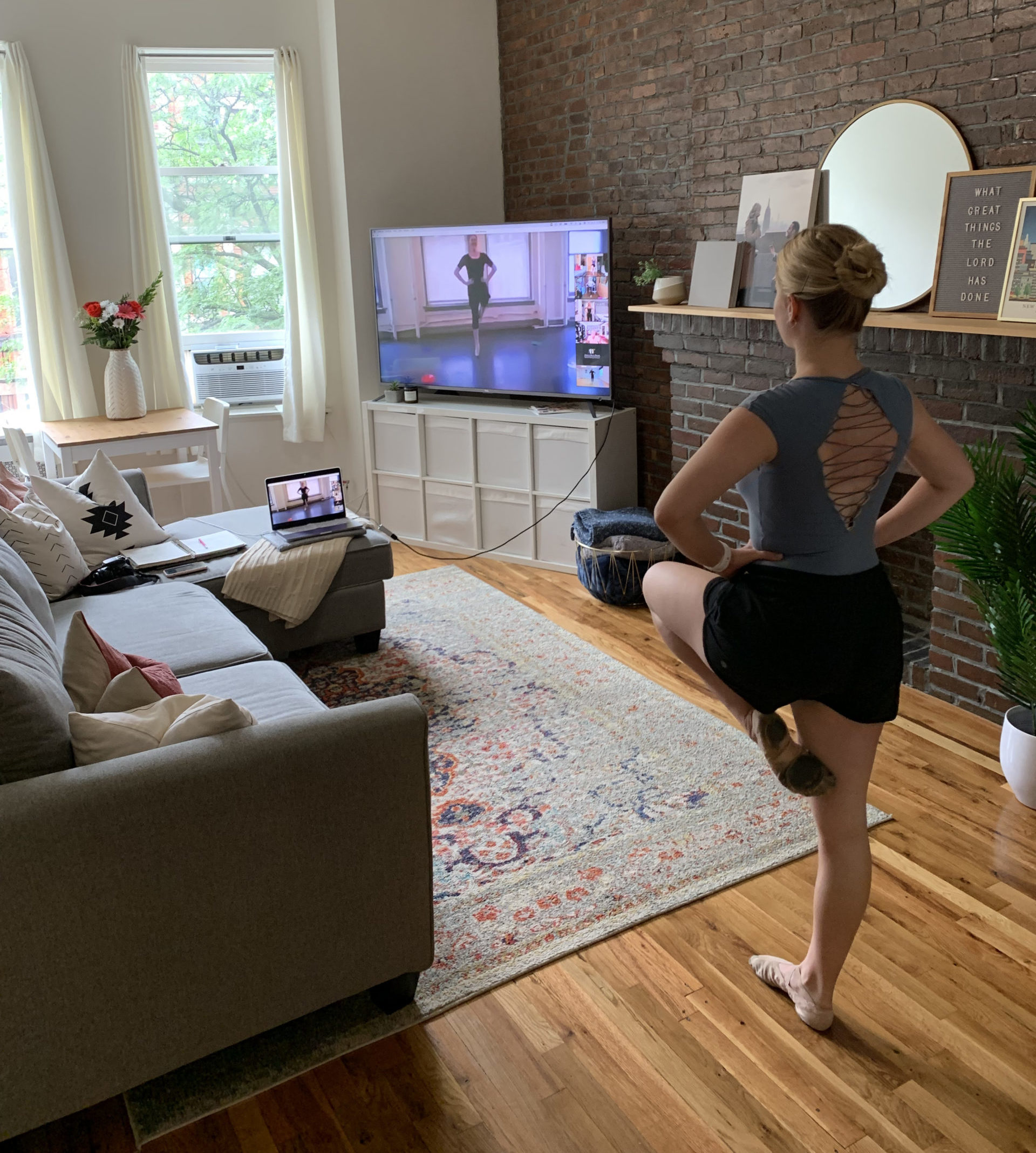Haley Hilton takes a ballet class from her living room. She balances in passe, hands on hips, looking at her television where her teacher is on Zoom.