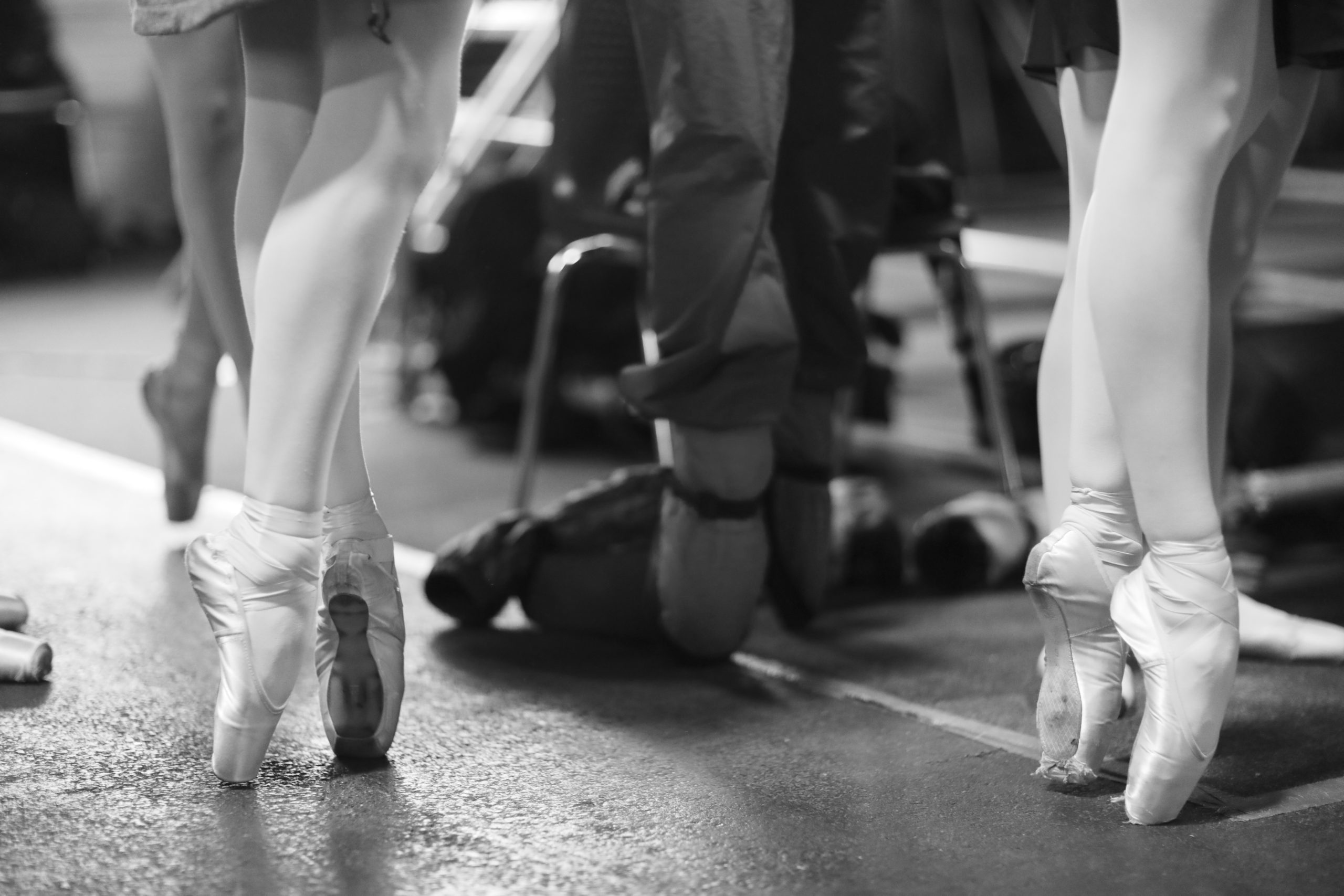 Black and white image of legs of ballerinas standing on pointe shoes at the rehearsal of the performance