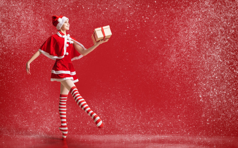 Dancing ballerina girl in pointe shoes with gift in her hands dressed as Santa Claus on red background