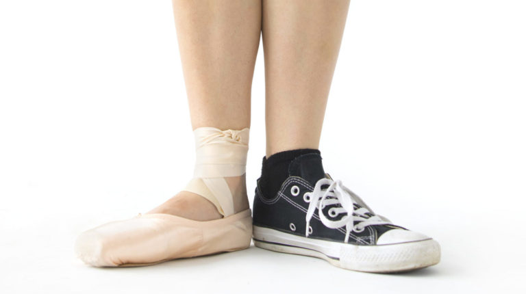 Image of a dancer's legs with a ballet shoe on one foot and sneakers on the other