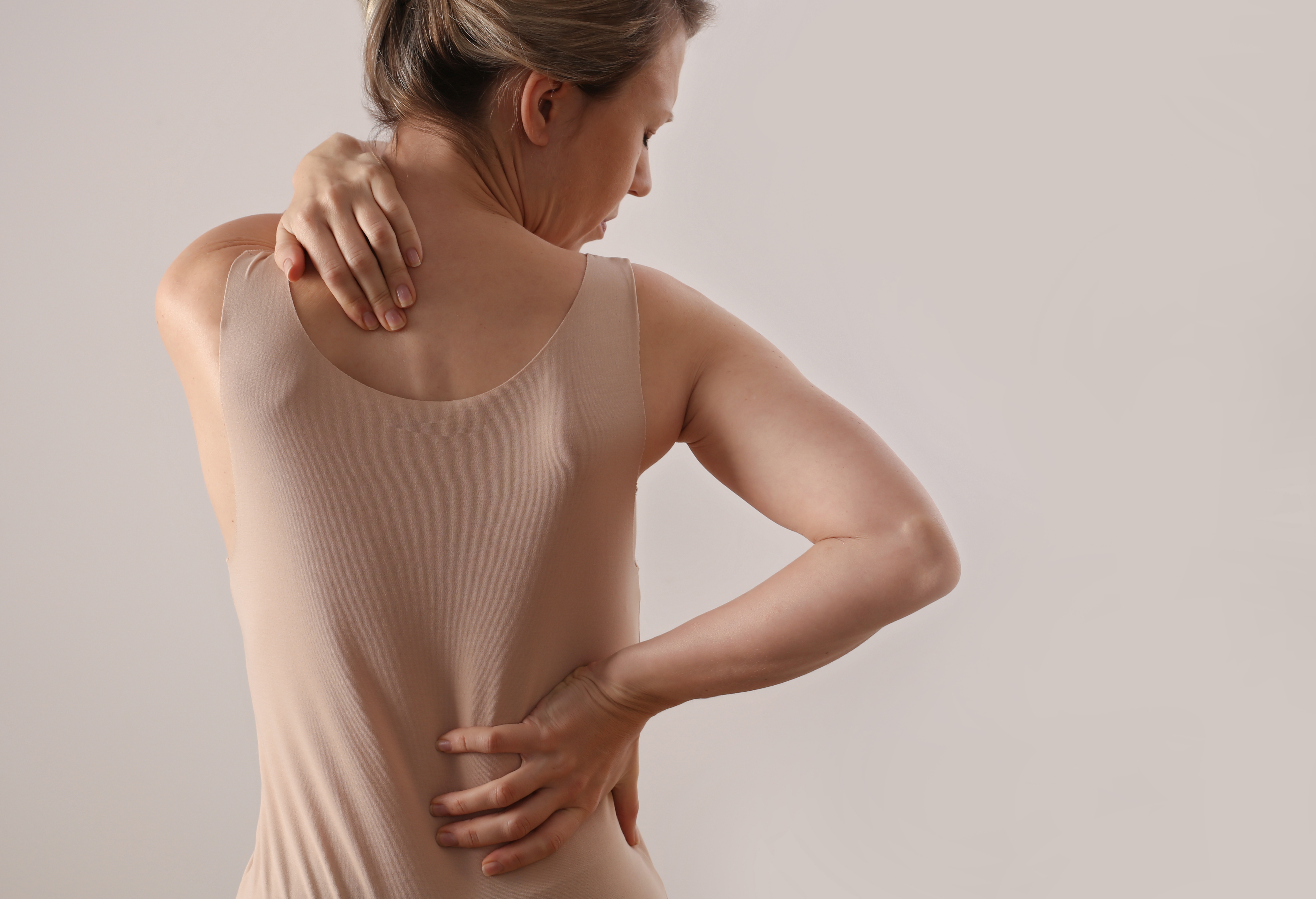 A woman with back pain and scoliosis. She is clutching her low back and neck.