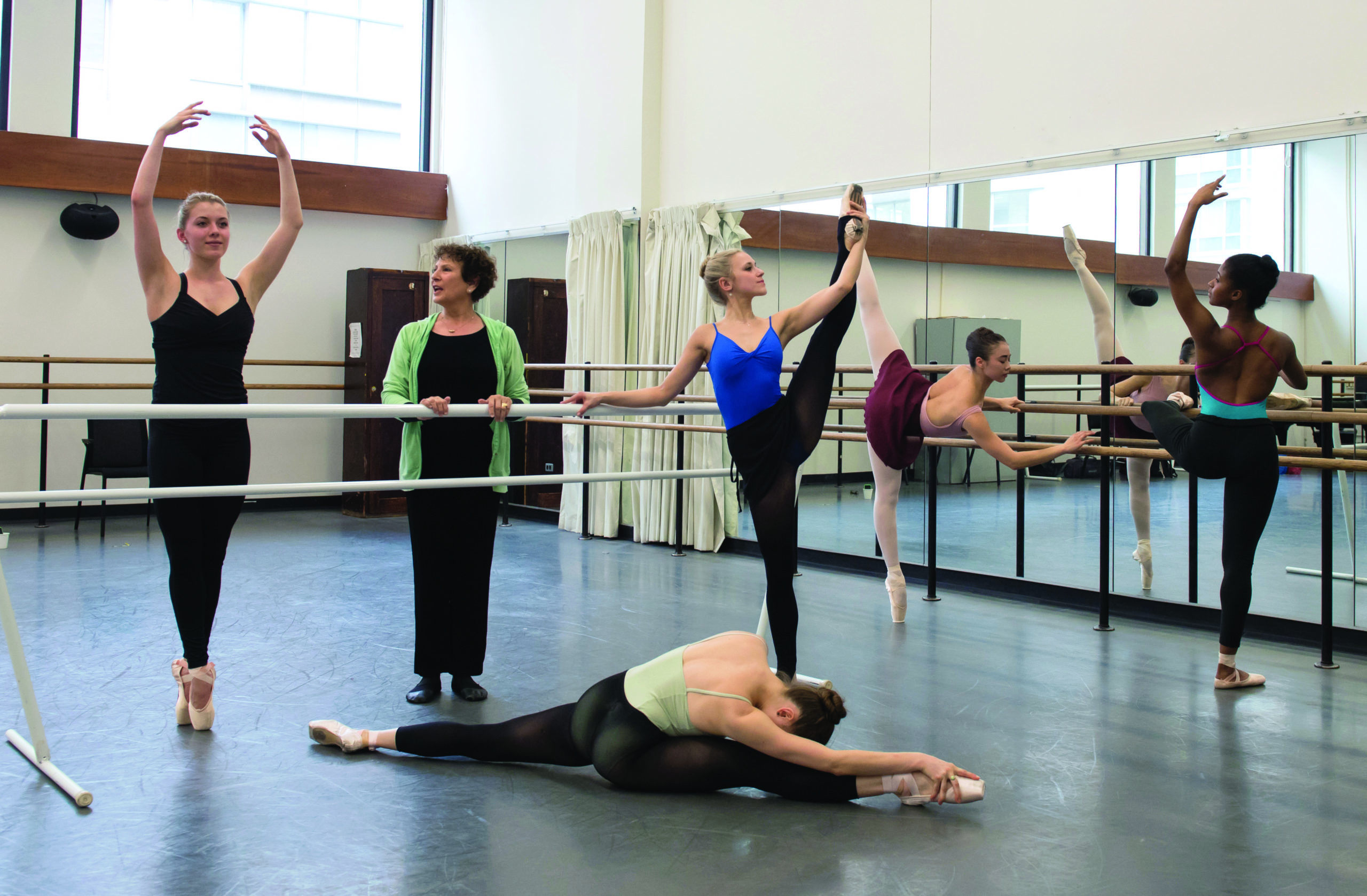 Group of dancers stretching around the barre with a dance educator Charla Genn in the middle