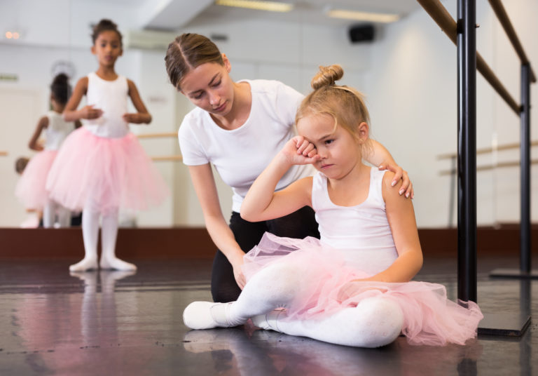 Female ballet teacher supporting little upset girl in studio