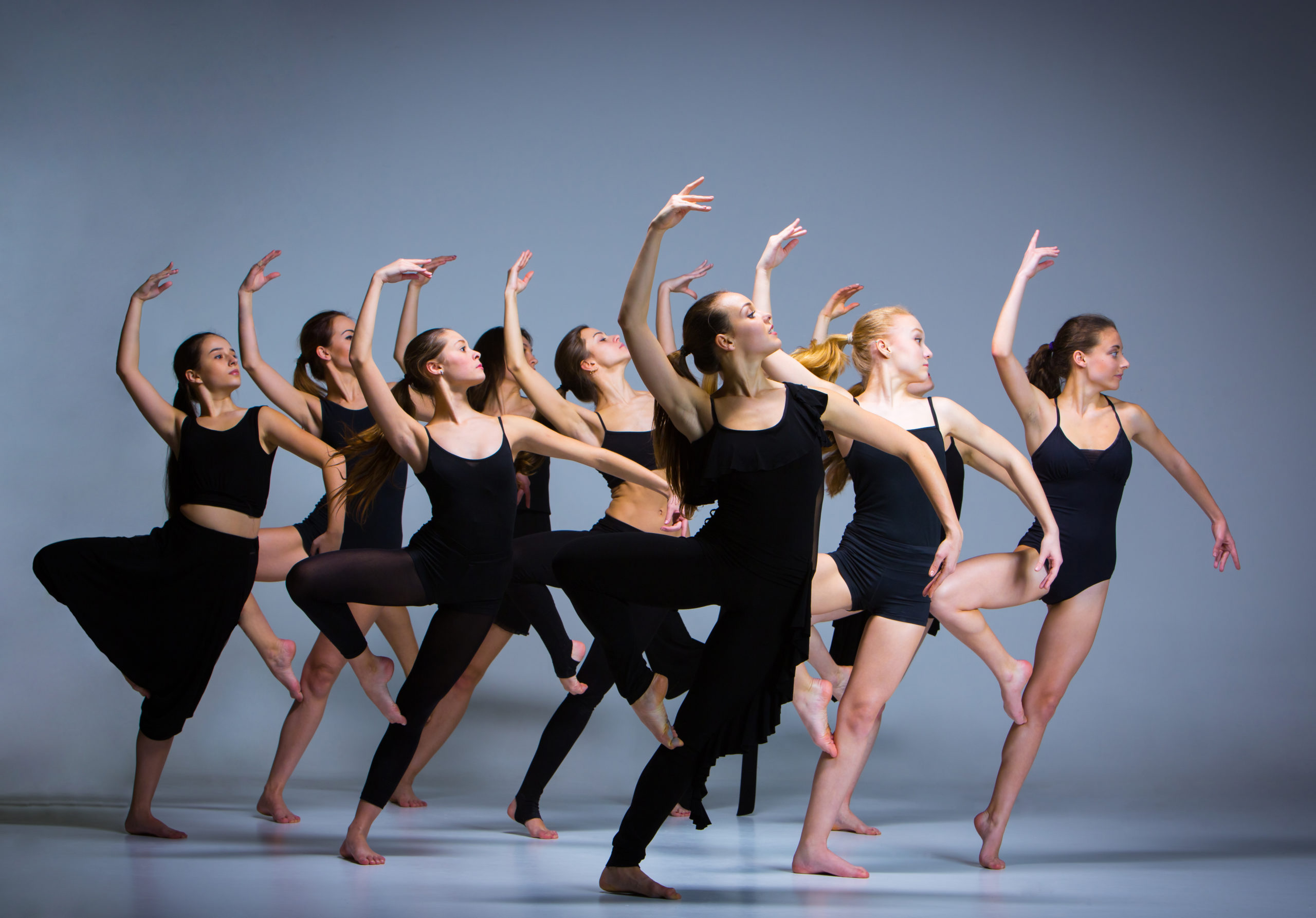 Group of modern ballet dancers dancing in front of a gray background