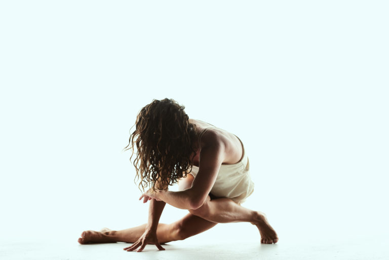Image of Chelsea Ainsworth holding a dance pose (her face unseen) against a light blue background