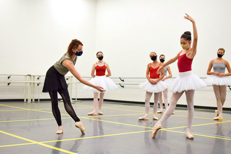 Female instructor assisting a young ballet dancer in the studio