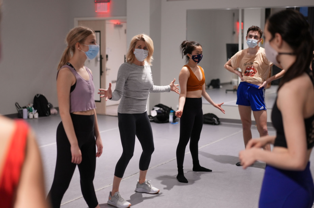 Laurie Kanyok stands in a line of young adult students wearing athletics wear. They all face the front of the room with their palms turned forward, working on an acting exercise.