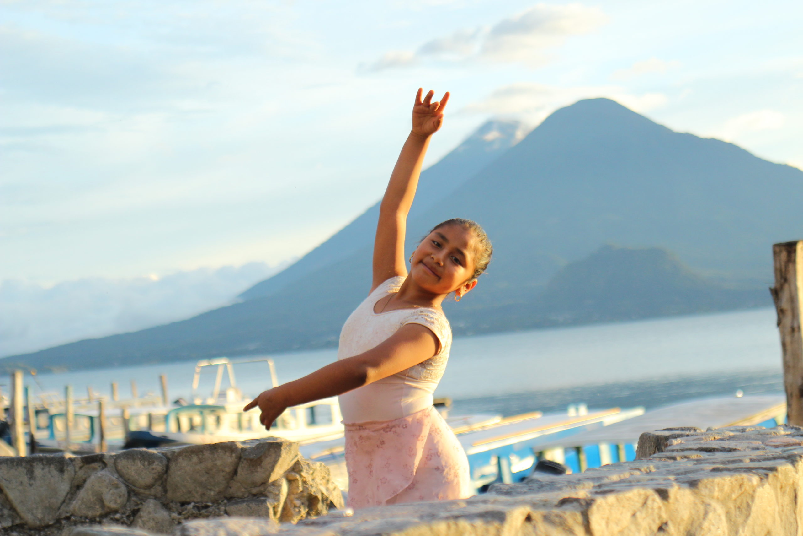 Image of a young ballerina standing outdoors in fourth position with a river and mountains behind her