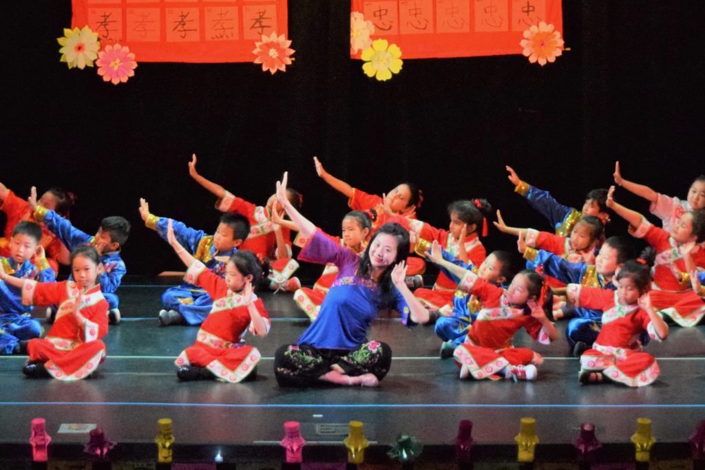 Dance teacher and students seated and performing a Chinese traditional dance on stage