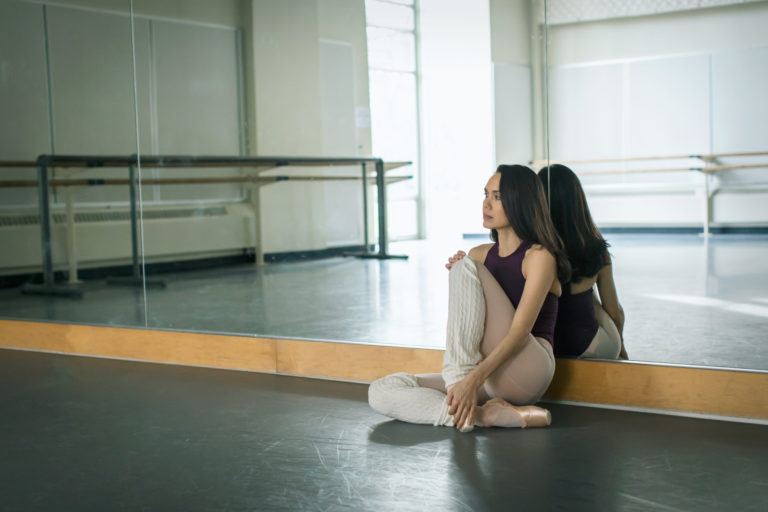 Ballet dancer sitting on the floor against a mirror in a dance studio