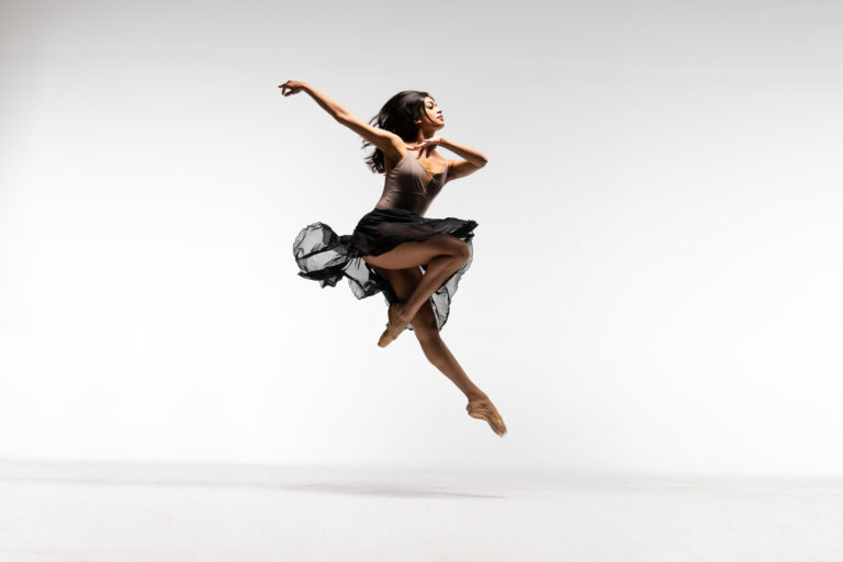 Dancer in brown costume leaping in the air against a white background