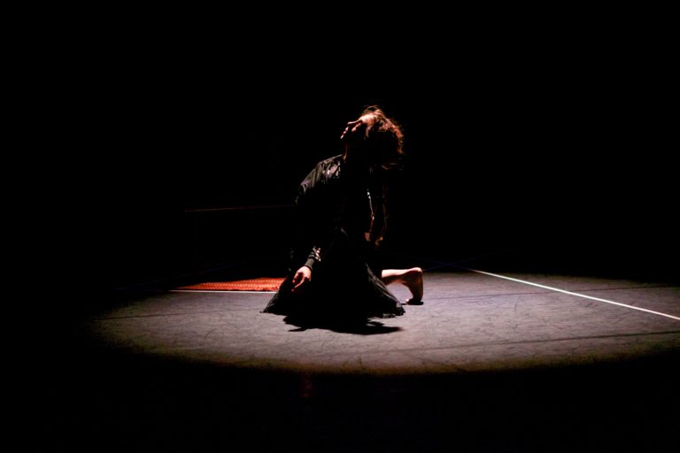 A dancer performs on the floor, illuminated by a spotlight within a dark room.