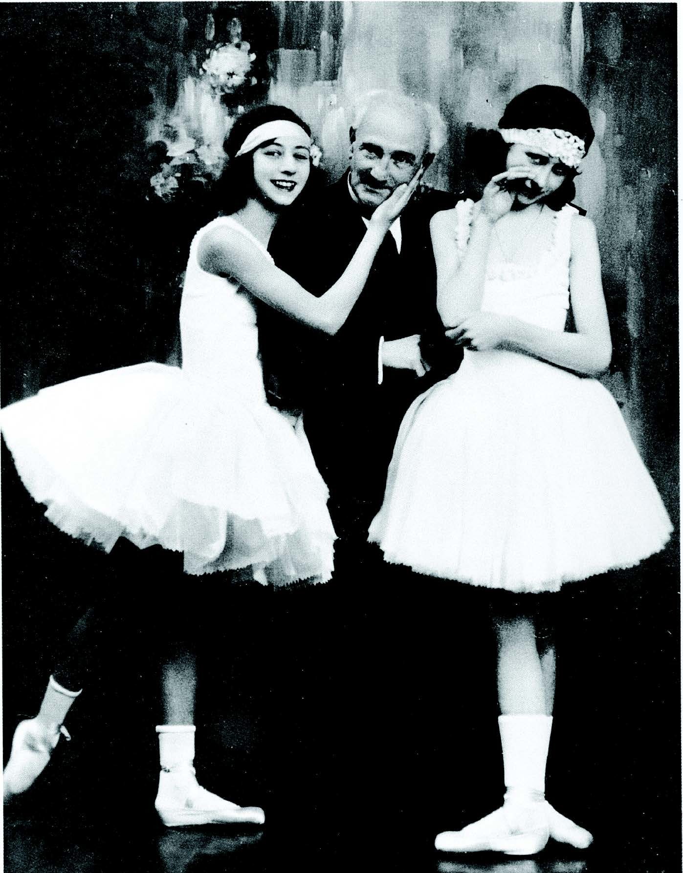 Smiling and posing for a picture, two ballerinas in tutus stand on either side of a man in a suit.