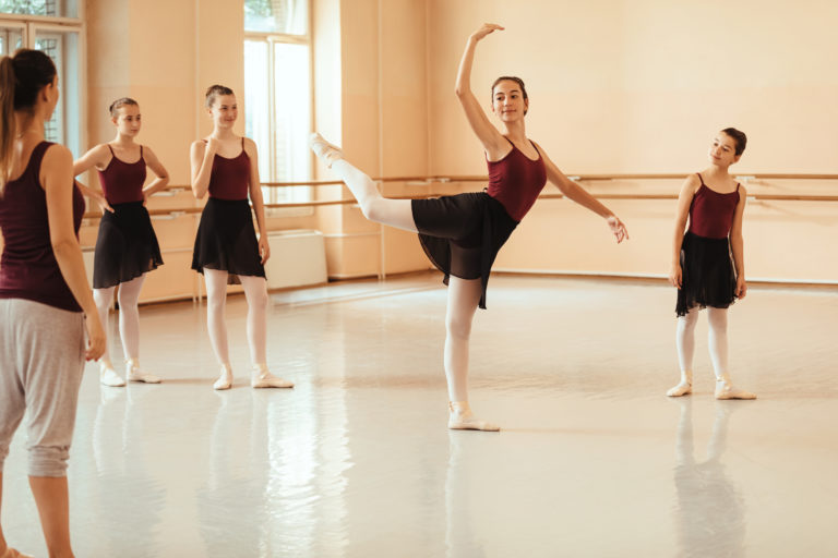 Group of ballerinas practicing with instructor at ballet studio. Focus is on ballerina dancing in the middle.
