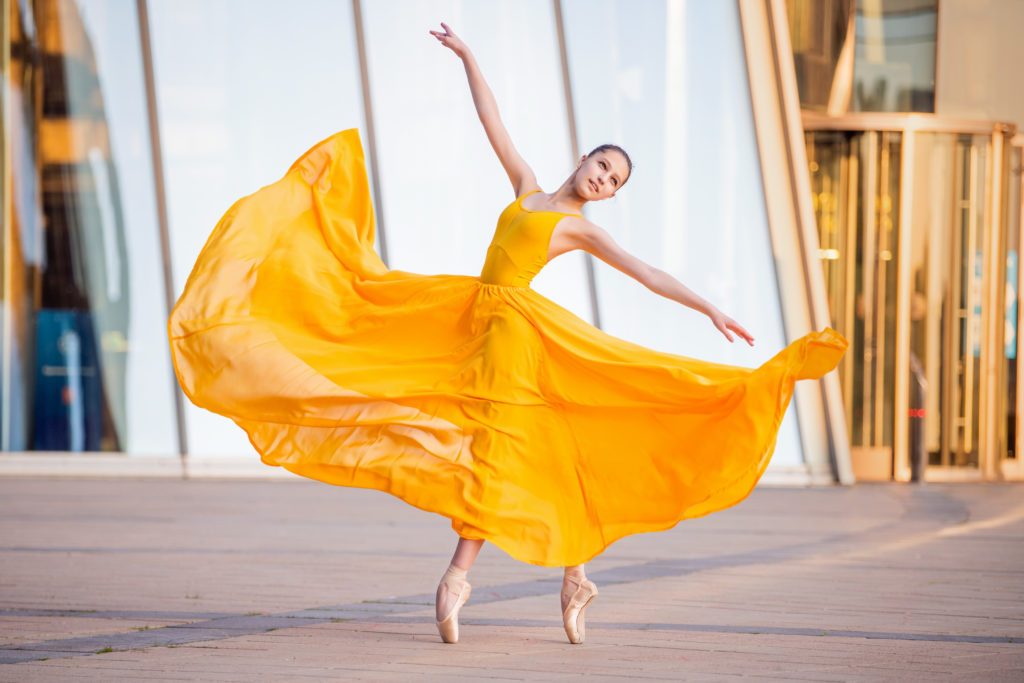 young ballerina in a long flying yellow dress is dancing against the backdrop of cityscape