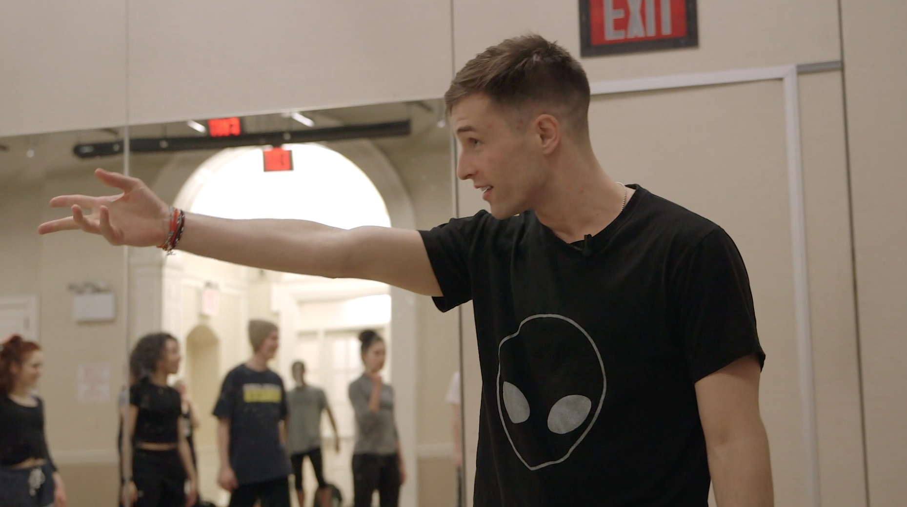 A dance teacher gestures across the room with his arm.